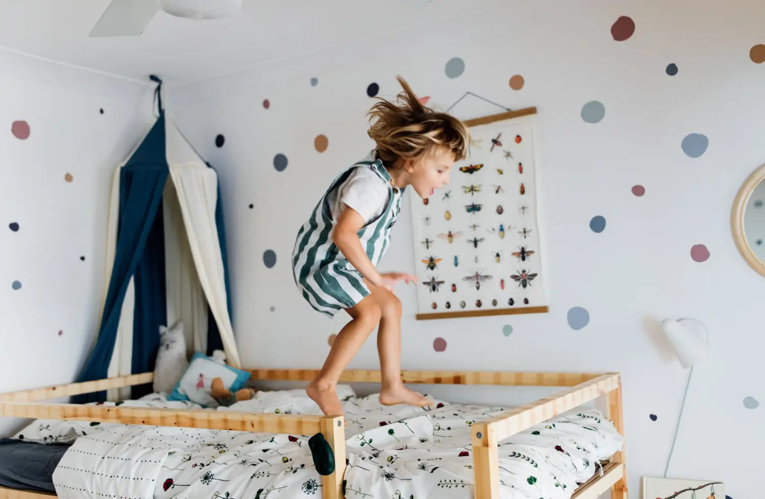 Child jumping on bed with colorful polka dot wall stickers