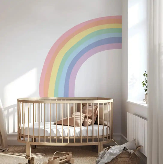 Oval wooden crib with a painted rainbow on the wall above it.