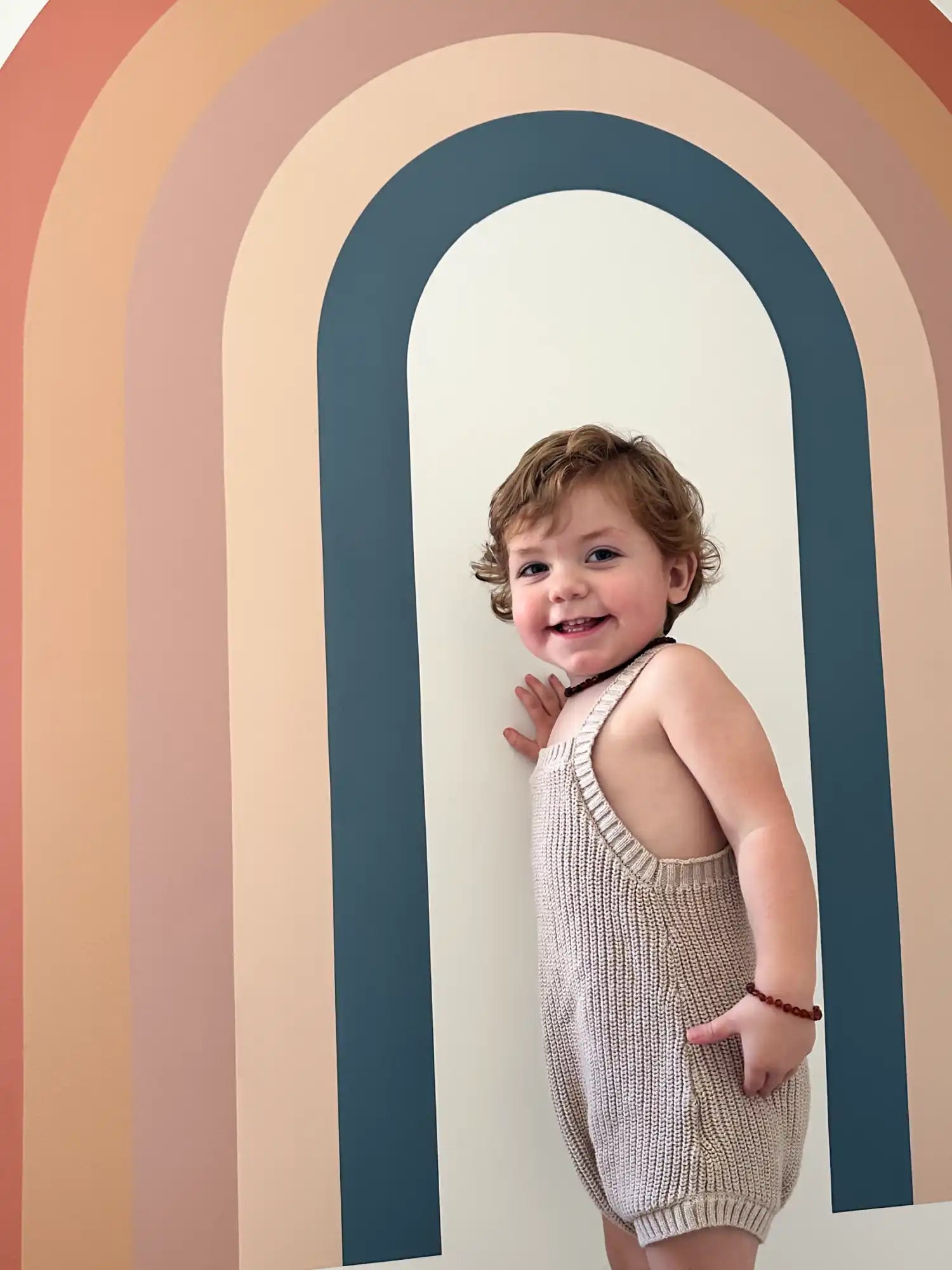 A smiling toddler in a knitted romper.