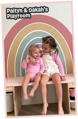 Two young girls in a playroom with a rainbow mural