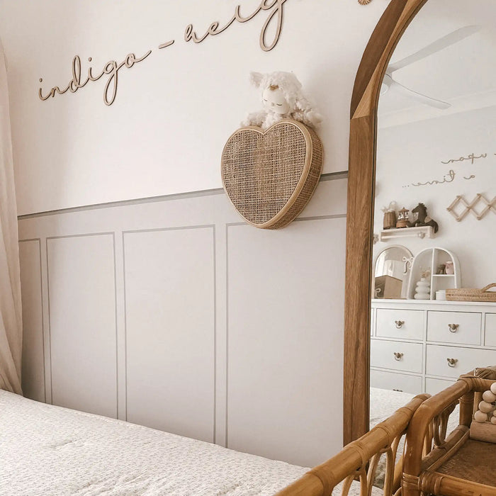 A woven heart-shaped wall shelf with a small stuffed animal.
