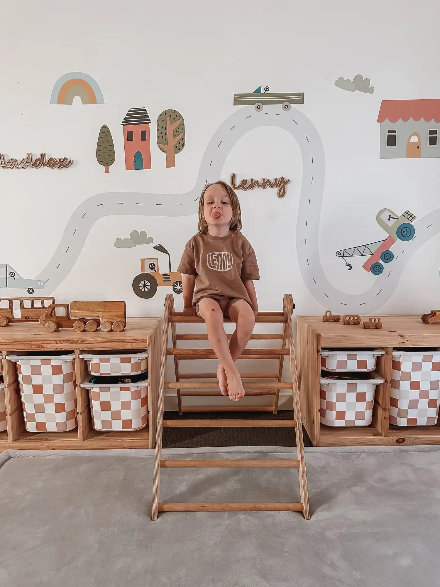 A young child in a brown outfit sitting on a wooden climbing triangle.